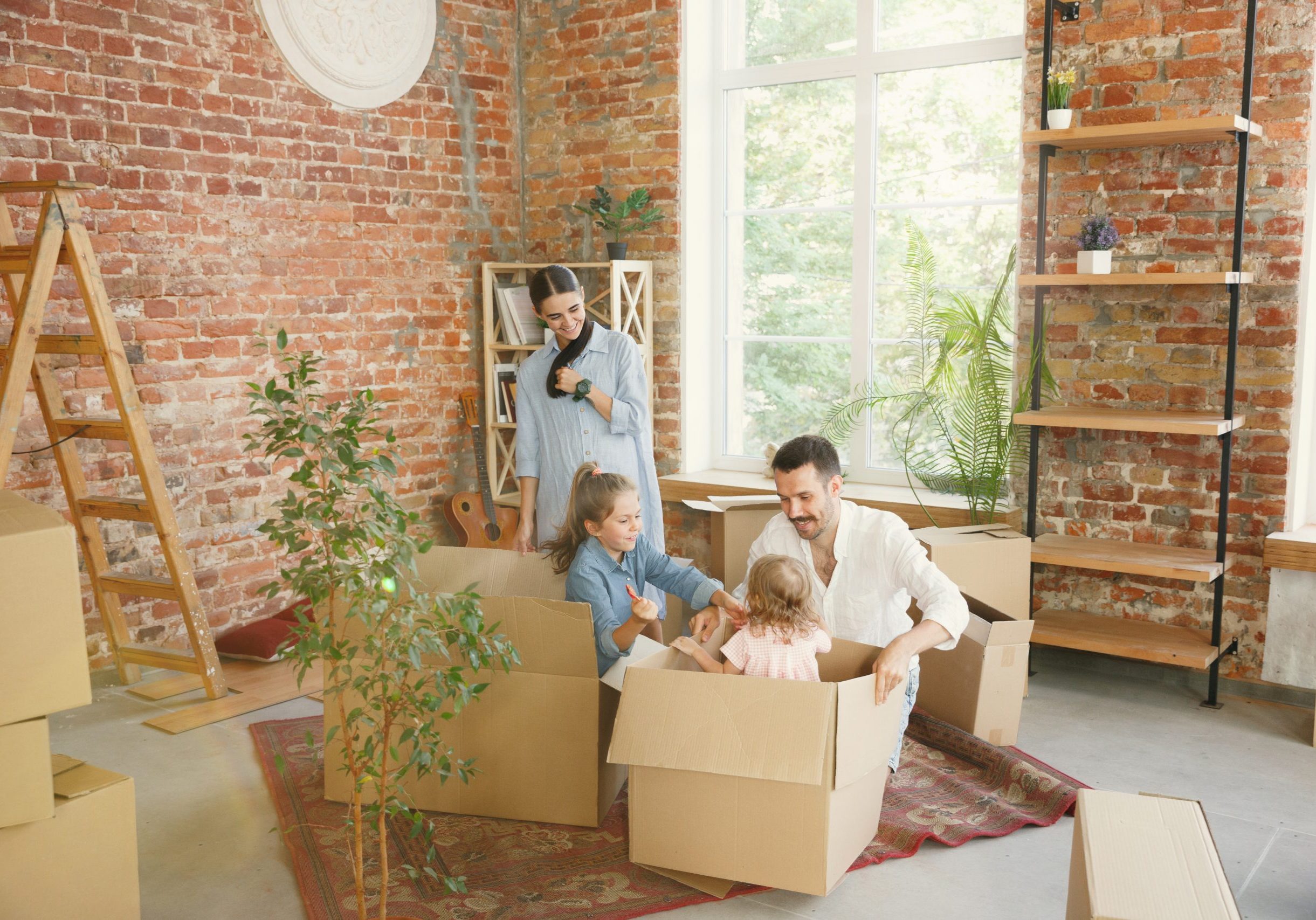 New life. Adult family moved to a new house or apartment. Spouses and children look happy and confident. Moving, relations, new life concept. Unpacking boxes with their things, playing together.