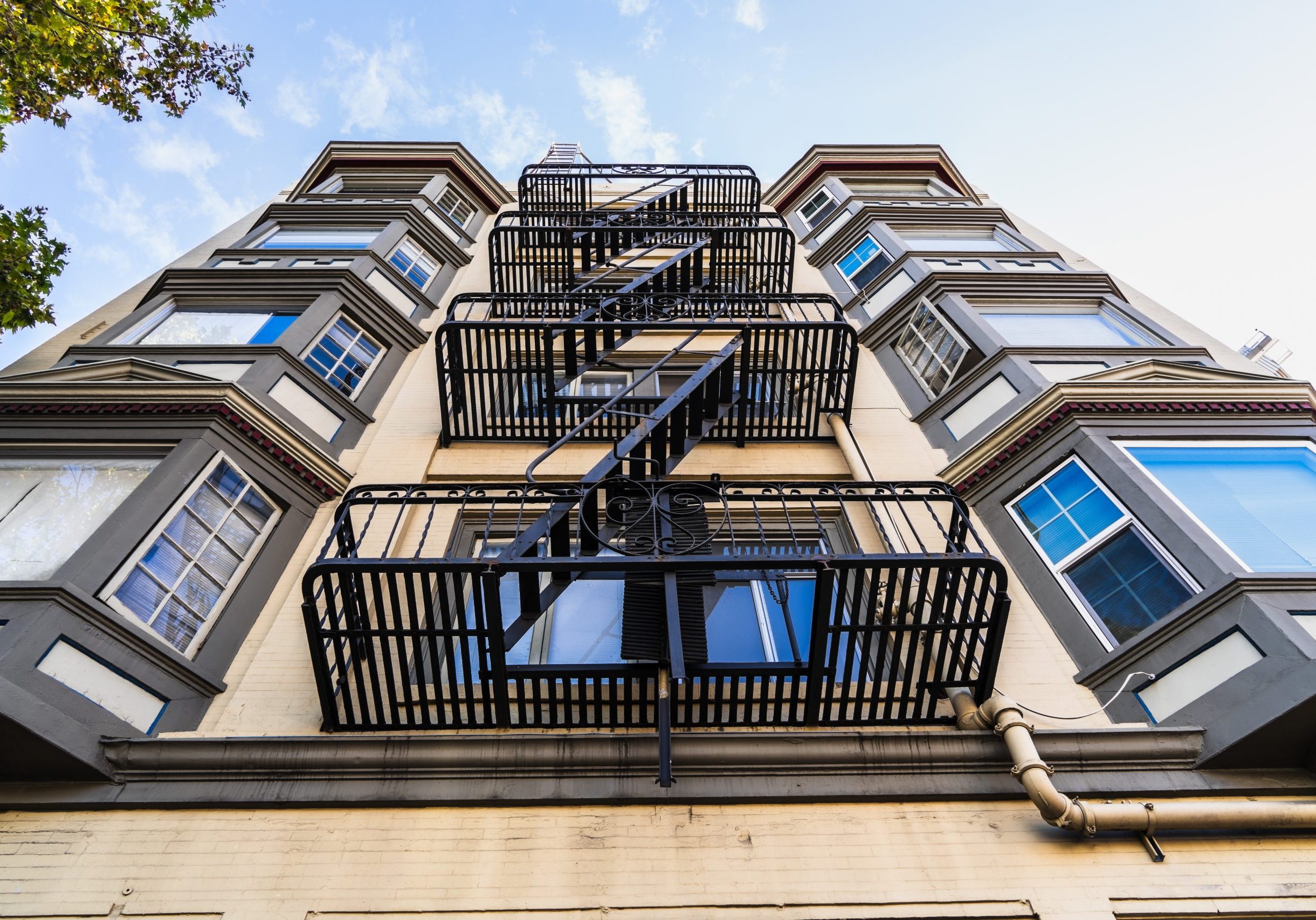 Exterior view of multifamily residential building; Old metal fire escape stairs hanging on side of the building; Berkeley, San Francisco Bay Area, California